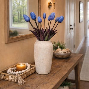 May include: A wooden console table with a vase of blue tulips. A lit candle sits on a woven tray with decorative beads. A wooden bowl with decorative spheres and a mirror are in the background.
