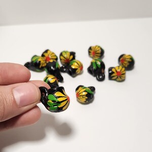 May include: A group of small black ceramic jugs with yellow and green floral designs. The jugs have a small loop handle and are painted with a black outline.