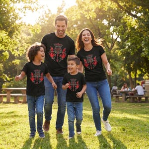 May include: Black short-sleeve t-shirts featuring a red and grey thistle graphic on the chest. The shirts are worn with blue denim jeans. The graphic depicts a stylized floral thistle design with sharp, pointed leaves and a central bloom.