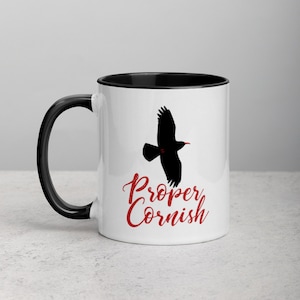 May include: White ceramic mug with a black rim and handle. The mug features a black silhouette of a bird in flight with the text "Proper Cornish" in red lettering.