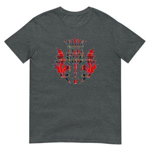 May include: A dark heather gray short-sleeve t-shirt featuring a central graphic of a thistle plant. The thistle design is filled with a red, yellow, and blue plaid tartan pattern, showcasing sharp, jagged leaves and a spiky, rounded flower head.