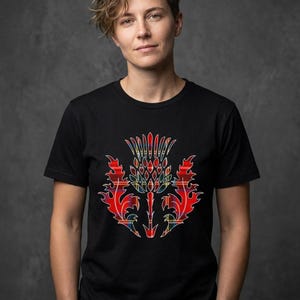 May include: A black short-sleeved t-shirt featuring a central graphic of a thistle plant. The thistle design is filled with a red, yellow, and blue plaid tartan pattern, showcasing sharp, flame-like leaf edges and a textured, rounded flower head.