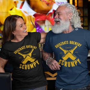 May include: Two people wearing black and blue t-shirts with a graphic design of crossed beer bottles and the text "Rufazrats Brewery Cornish Est 1553 Scrumpy".