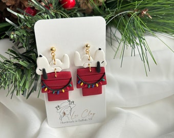 Puede incluir: Pendientes de Snoopy hechos a mano. Los pendientes presentan a Snoopy encima de su caseta roja, decorada con luces navideñas. Los pendientes son blancos, rojos, negros y dorados. Los pendientes están sujetos a una tarjeta blanca con el texto "Lee Clay Handmade in Buffalo NY".