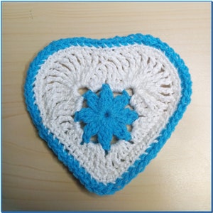 May include: A white crocheted heart-shaped coaster with a blue crocheted flower in the centre.