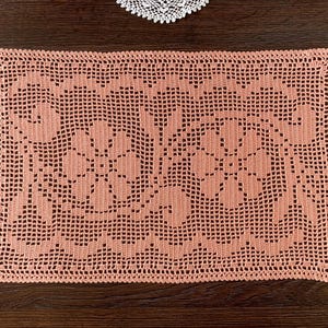 May include: A rectangular, peach-colored crochet doily with a floral pattern. The openwork design features repeating flower motifs and a scalloped edge. The doily is handmade and suitable for home decor.
