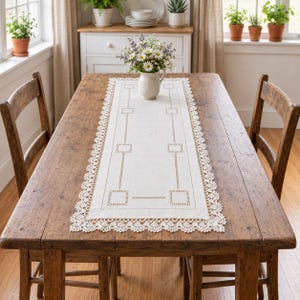 May include: A rectangular off-white table runner featuring intricate cutwork embroidery, geometric square patterns, and a scalloped lace border. The runner is centered on a rustic wooden table and holds a white ceramic pitcher filled with daisies.