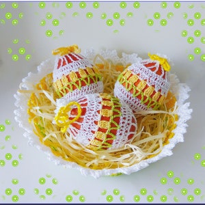 May include: Three crocheted Easter eggs in a white crocheted basket with yellow straw. The eggs are red, white, and yellow.