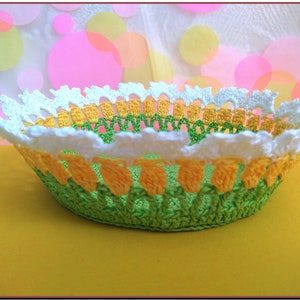 May include: A crocheted bowl with a white, yellow, and green design. The bowl is made of yarn and has a scalloped edge.