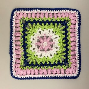Könnte beinhalten: Ein gehäkeltes Quadrat mit einem Blumendesign in den Farben Rosa, Grün, Weiß und Blau.