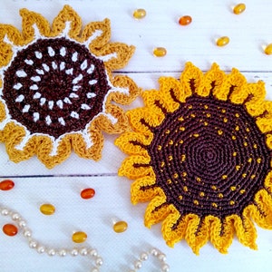 Pode incluir: Duas bases de copo de girassol de crochê feitas à mão. As bases de copo apresentam um esquema de cores amarelo e marrom, com designs detalhados de pétalas e centro. Contas decorativas e um colar de pérolas estão espalhados.