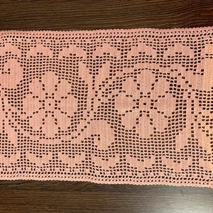 Peut inclure: Un napperon rectangulaire en crochet de couleur pêche présentant un motif ajouré complexe composé de deux grandes fleurs centrales entourées de motifs de feuilles et de vignes. La pièce possède une bordure festonnée et une structure en grille.