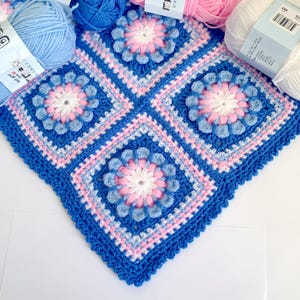 May include: A crocheted baby blanket with a blue, pink, and white floral pattern. The blanket is made with a soft yarn and has a delicate texture.