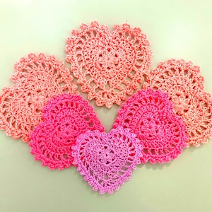 May include: Five crocheted heart-shaped doilies in shades of pink and light pink.