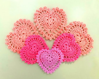 Peut inclure: Cinq napperons en crochet en forme de cœur dans des tons de rose et de rose clair.