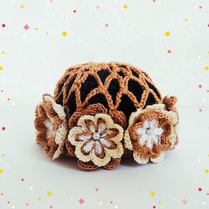 May include: A brown crocheted hairnet with three crocheted flowers attached. The flowers are beige and white with a pearl bead in the center.