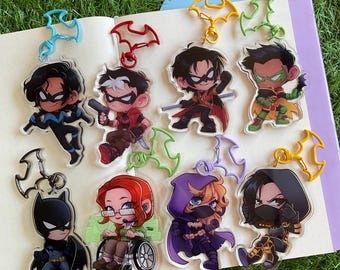 Può includere: Collezione di portachiavi in acrilico con vari personaggi dei fumetti. Ogni portachiavi presenta un'illustrazione del personaggio con una chiusura a forma di pipistrello. I personaggi includono Batman, Robin e altri, in colori vivaci.