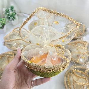 May include: A set of small, decorative bowls with gold trim and a sheer, white fabric lining. The bowls are filled with orange-colored items and have a green base.