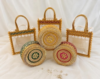 May include: Two square tote bags with gold trim and white lace, and three round containers with gold embroidery. One round container is gold, one is green, and one is magenta. Each round piece features a central floral motif and gold fringe.