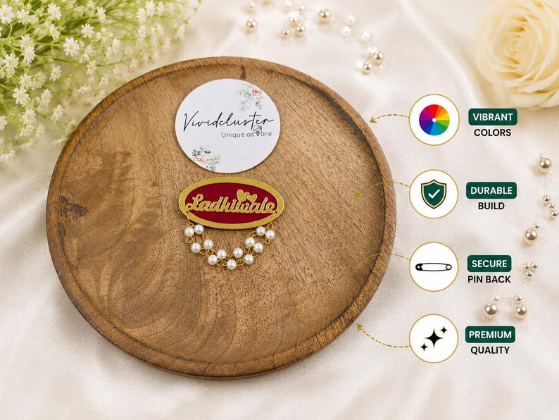Puede incluir: Un broche de forma ovalada con un centro rojo intenso, el texto dorado 'Ladkiwale' y dos peque&ntilde;os corazones dorados. El broche est&aacute; adornado con dos hileras de perlas blancas artificiales y un marco de metal dorado con un cierre de seguridad.