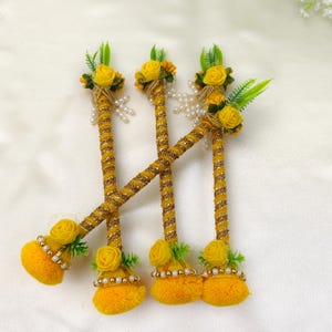 May include: Three decorative sticks wrapped in gold glitter ribbon, each topped with a yellow foam rose, green plastic leaves, and white faux pearl accents. The base of each stick features a yellow pom-pom, a yellow foam rose, and pearl trim.