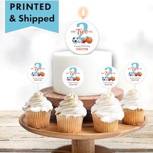 May include: A white frosted cake with a lit candle shaped like the number 2, and cupcake toppers. The candle and toppers feature sports balls and the text "Happy Birthday Easton". The image also includes the text "PRINTED & Shipped".