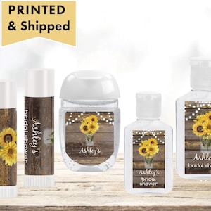 May include: Set of four personalized hand sanitizer bottles and lip balm tubes with a rustic wood background and sunflower design. The labels say "Ashley's Bridal Shower".
