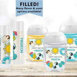 May include: Set of four personalized hand sanitizers and lip balms with a summer theme. The labels feature a sun, beach ball, sunglasses, and flip flops. The text on the labels reads "Happy Birthday Madison".