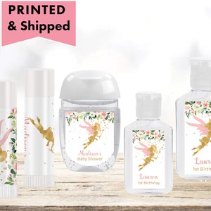 May include: Set of five hand sanitizer bottles and lip balm tubes with personalized labels featuring a gold fairy with pink wings and floral accents. The labels include the names "Madison's Baby Shower" and "Lauren 1st Birthday".