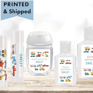 May include: Four personalized hand sanitizer bottles and two lip balm tubes with labels featuring a construction theme. The labels have a blue, yellow, red, and white color scheme and feature a variety of construction vehicles. The text on the labels reads "Happy Birthday Oakley".