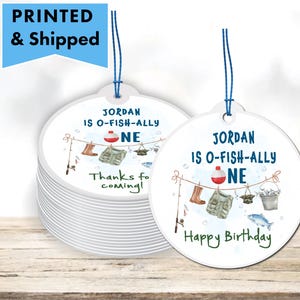 May include: Round white favor tags with blue and green fishing themed illustrations. The text reads "Jordan is O-Fish-Ally One" and "Happy Birthday".