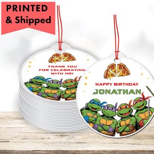 May include: White, round ornaments featuring the Teenage Mutant Ninja Turtles with pizza slices and text. One ornament says "Happy Birthday Jonathan" and another says "Thank you for celebrating with me!" Each has a red string.