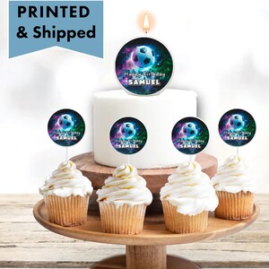 May include: A birthday cake with a soccer ball candle on top. There are cupcakes with soccer ball toppers around the cake. The toppers say "Happy Birthday Samuel".