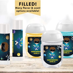 May include: Four clear plastic bottles with labels featuring a space-themed design. The labels have a blue, black, and yellow background with a cartoon astronaut holding a video game controller. The text on the labels reads "Noah Reached Level 11".