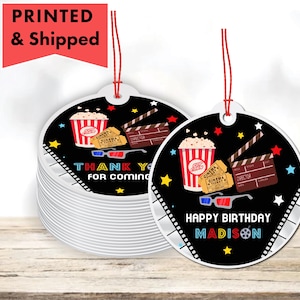 May include: Two round black and white favor tags with a movie theme. One tag says "Thank you for coming" and the other says "Happy Birthday Madison". Both tags have popcorn, movie tickets, and a clapperboard.
