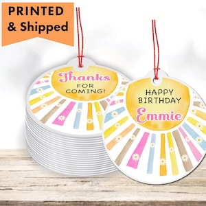 May include: Two round, colorful gift tags with a sunburst design. One tag says "Thanks for coming!" and the other says "Happy Birthday Emmie".