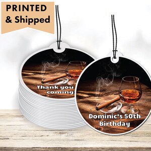 May include: Two round, white, printed gift tags with black string. The tag on the left says "Thank you coming". The tag on the right says "Dominic's 50th Birthday". Both tags feature a brown wooden surface with a glass of amber liquid and a brown cigar.