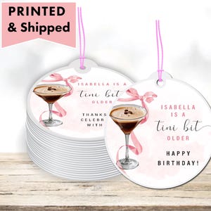 May include: White round gift tags with a pink ribbon and a cocktail illustration. Text on the tag reads "Isabella is a tini bit older" and "Happy Birthday!". The words "Printed & Shipped" are in a pink banner.