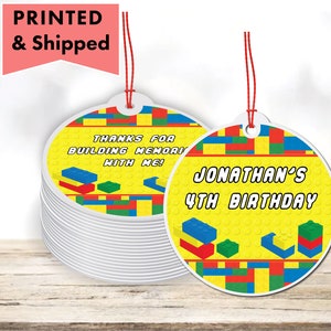 May include: A stack of round, yellow birthday party favor tags with red string. The tags feature colorful block designs and text that reads "Jonathan's 4th Birthday" and "Thanks for building memories with me!"