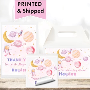 May include: White party favor boxes and cards with a space theme. The design includes planets, rockets, astronauts, and moons in pink, orange, and purple. Text on the boxes reads "Thank you for celebrating with me!" and a name.