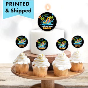 May include: A birthday cake with a water slide theme, featuring a lit candle and cupcake toppers. The cake and cupcakes have a black and colorful design with the text "HAPPY BIRTHDAY HAYDEN". The image also includes the text "PRINTED & Shipped".