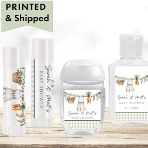 May include: A collection of baby shower favors, including lip balm, hand sanitizer, and a small pump bottle. Each item features a label with a watercolor design of a baby dress, carrots, and the text "Sarah & Matt's BABY SHOWER". The words "PRINTED & Shipped" are at the top.