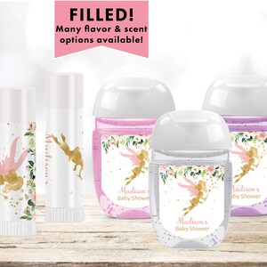 May include: Four small bottles of hand sanitizer with labels featuring a fairy design and the text "Madison's Baby Shower". The bottles are on a wooden surface.