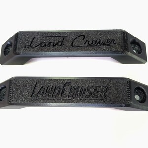 May include: Two black plastic door handles with the text "Land Cruiser" embossed on them.