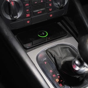 Könnte beinhalten: Ein schwarzer Innenraum eines Autos mit einem kabellosen Ladegerät und einem Schalthebel. Das Ladegerät hat eine grüne Leuchte, die anzeigt, dass es aktiv ist. Der Schalthebel hat die Buchstaben P, R, N, D und S.