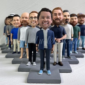 May include: A group of custom-made figurines of people standing in a line on gray bases. The figurines are all wearing different clothing and have realistic facial features.