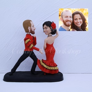 May include: A custom-made cake topper featuring a couple in a dancing pose. The man is wearing a red and black outfit, and the woman is wearing a red dress with gold trim. The couple is posed as if they are dancing the tango. The cake topper is a great way to personalize a wedding cake or anniversary cake.