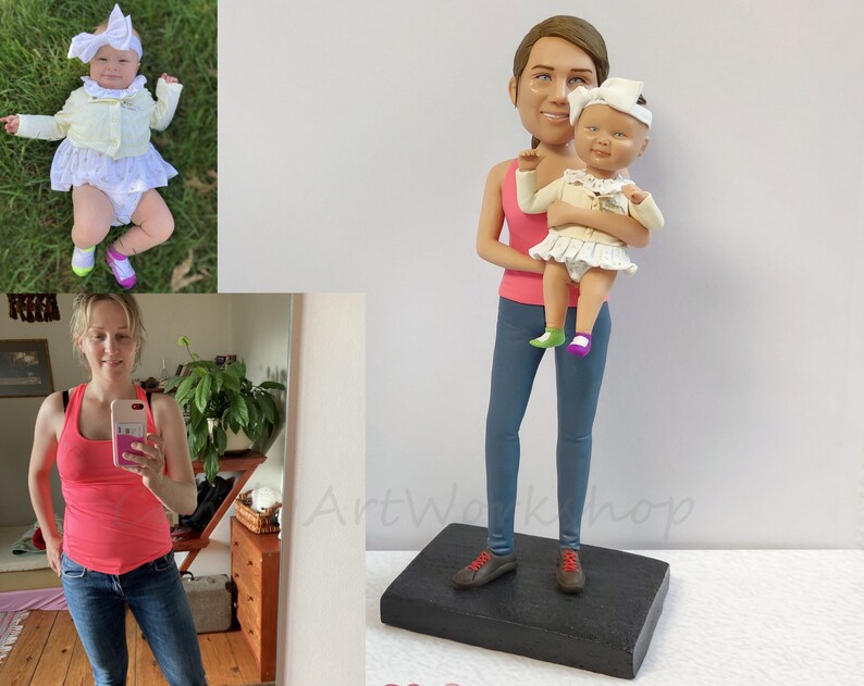May include: A custom-made figurine of a woman holding a baby. The woman is wearing a pink tank top and blue jeans. The baby is wearing a white dress and a white headband. The figurine is standing on a black base.