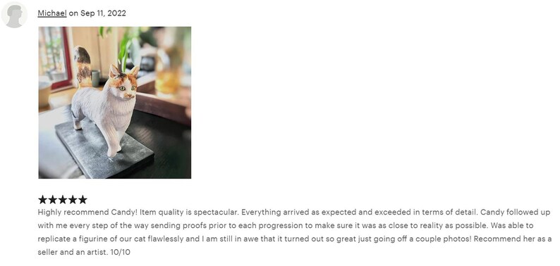 May include: A white, gray, and orange cat figurine with a black base. The figurine is a replica of a customer's cat.