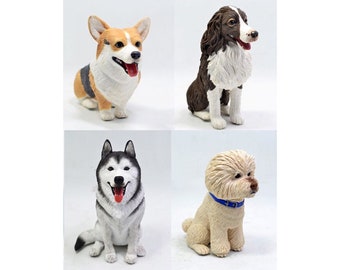 May include: A set of four dog figurines including a tan and white Corgi, a brown and white spaniel-type dog, a black and white Husky with a red tongue, and a cream-colored curly-haired dog wearing a blue collar, all in a sitting position.